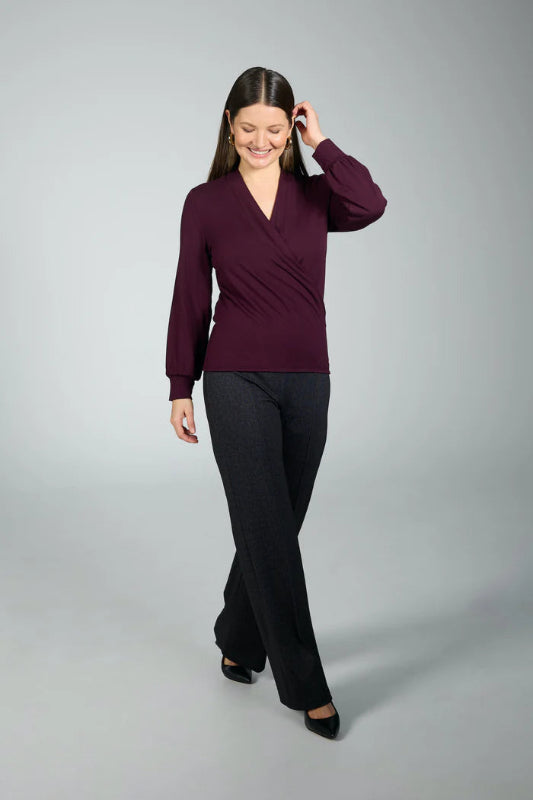 Woman wearing a purple top and black pants on a gray background