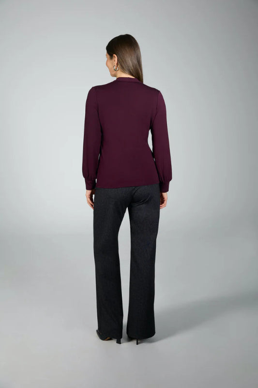 Woman wearing a purple long-sleeve top and black pants on a gray background