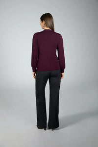 Woman wearing a purple long-sleeve top and black pants on a gray background