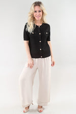 Load image into Gallery viewer, Woman wearing a black button-up shirt and beige pants on a white background
