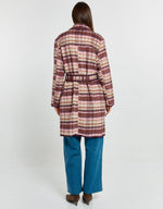 Load image into Gallery viewer, A woman viewed from the back wearing a long plaid coat in muted pink, burgundy, and cream tones, paired with wide-leg blue jeans and brown pointed shoes, against a plain light gray studio background.
