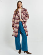 Load image into Gallery viewer, A woman models a mid-length plaid coat in burgundy, beige, and cream tones, paired with wide-leg blue jeans and brown pointed-toe ankle boots, against a plain light gray studio background.
