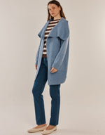 Load image into Gallery viewer, A woman modeling a cornflower blue open-front coat over a brown and white striped top, blue jeans, and beige flats, photographed against a plain light beige studio background.
