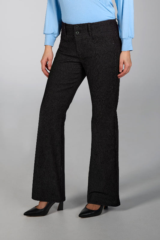 Person wearing black boot cut  pants and a light blue top on a gray background
