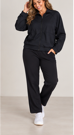 Load image into Gallery viewer, A woman modeling a matching black zip-up jacket and wide-leg pants set, paired with white sneakers, against a neutral studio background.
