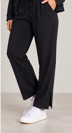 Load image into Gallery viewer, Black wide-leg drawstring pants with side slits, shown on a model wearing white sneakers against a neutral studio background.
