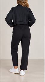 Load image into Gallery viewer, A woman shown from the back wearing a black cropped jacket and black pants, paired with white sneakers, against a neutral studio background.
