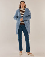 Load image into Gallery viewer, A woman modeling a cornflower 
blue open-front coat over a brown and white striped sweater, dark blue jeans, and beige flats, photographed against a plain light beige studio background.
