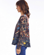 Load image into Gallery viewer, A woman shown in side profile wearing a long-sleeve, T-shirt with a complex multicolor print featuring leopard, tiger, and floral motifs on a dark background, paired with blue pants, against a plain white studio background.

