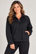 Load image into Gallery viewer, A woman wearing a black zip-up athletic jacket with side pockets and matching black jogger pants, photographed against a light gray studio background.
