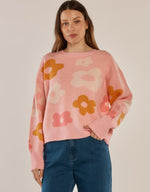 Load image into Gallery viewer, A woman wearing a pink crewneck sweater with a large floral pattern in orange, yellow, and cream, paired with blue jeans, against a plain beige background.
