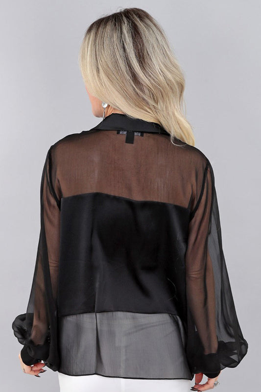 Woman wearing a black and sheer chiffon blouse against a gray background