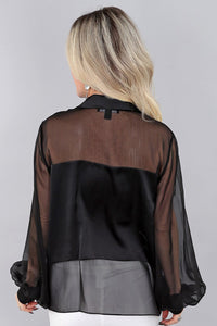 Woman wearing a black and sheer chiffon blouse against a gray background