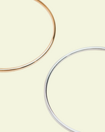 Load image into Gallery viewer, Two bracelets, one gold and one silver, on an off white background.
