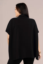 Load image into Gallery viewer, A woman shown from the back wearing a loose black draped top or cape with short wide sleeves, against a plain light beige studio background.
