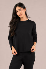 Load image into Gallery viewer, A woman modeling a black long-sleeve crewneck top and black pants against a solid light beige studio background.
