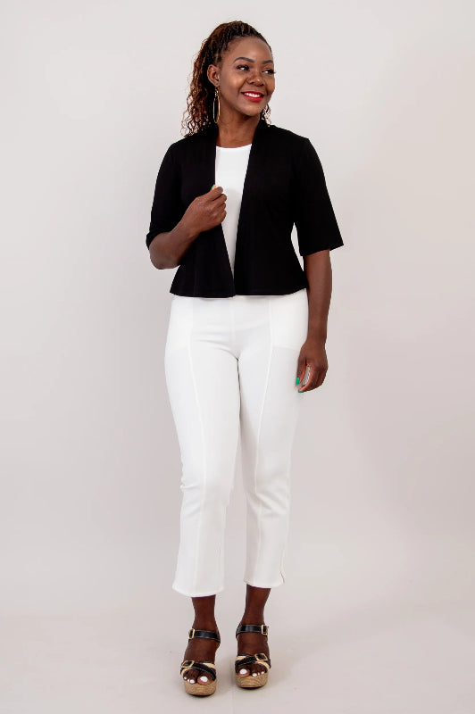 Woman wearing a black bolero, white top, and white pants on a plain background