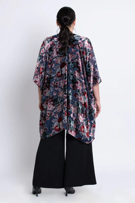 Woman wearing a floral velvet kimono over a black outfit on a white background