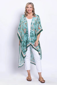 Woman wearing a long, green floral kimono over a white outfit on a white background