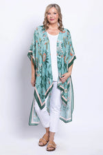 Load image into Gallery viewer, Woman wearing a long, green floral kimono over a white outfit on a white background

