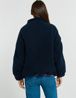 Load image into Gallery viewer, A woman viewed from the back wearing a dark navy blue sherpa fleece jacket and blue jeans against a plain light gray studio background.
