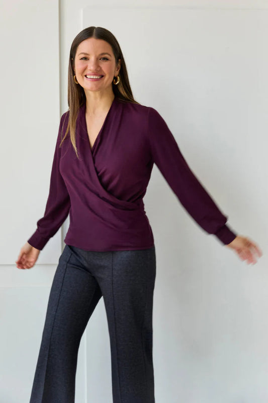 Woman wearing a purple top and dark pants against a white background