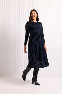 Woman wearing a dark blue  mesh and velvet dress with long sleeves, standing against a white background.
