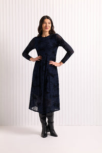 Woman wearing a dark blue  mesh and velvet dress with long sleeves, standing against a white background.