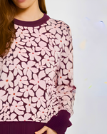 Load image into Gallery viewer, A close-up of a woman wearing a long-sleeve knit sweater with a pink and dark purple floral pattern, featuring solid dark purple ribbed collar, cuffs, and hem.
