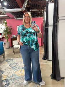 Person taking a mirror selfie wearing a tie-dye shirt and jeans in an indoor setting.