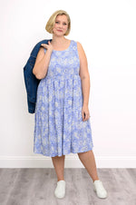 Load image into Gallery viewer, Woman wearing a blue floral dress holding a denim jacket against a white wall.
