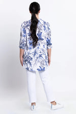 Load image into Gallery viewer, Woman wearing a blue floral patterned shirt and white pants on a white background
