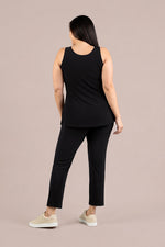 Load image into Gallery viewer, A woman shown from the back wearing a black sleeveless top and black cropped pants, paired with beige sneakers, against a solid light taupe background.
