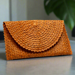 Load image into Gallery viewer, Orange woven clutch bag on a reflective surface with a blurred background
