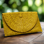 Load image into Gallery viewer, Yellow woven clutch bag on a wooden surface with a blurred green background
