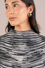 Load image into Gallery viewer, A close-up of a woman wearing a textured black and white striped Plisse Mock top and a gold-toned geometric earring, set against a solid beige background.
