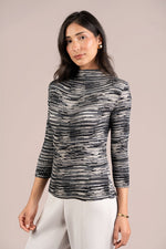 Load image into Gallery viewer, A woman modeling a black and white textured Plisse mock neck top with three-quarter sleeves, paired with white pants, against a solid beige background.
