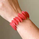 Load image into Gallery viewer, A red resin stretch bracelet with multiple elongated petal-like segments, shown worn on a person's wrist against a neutral beige background.

