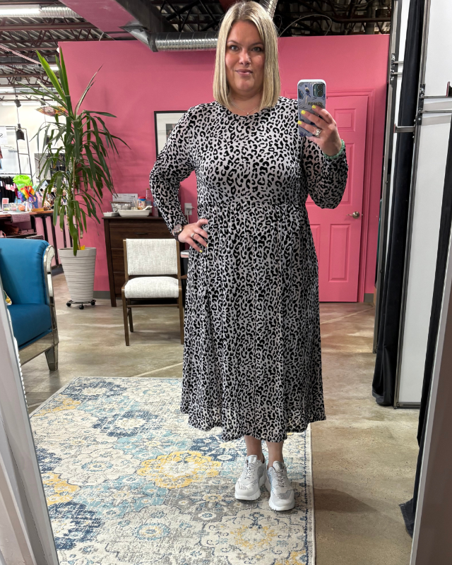 Woman taking a selfie wearing a grey mesh with velvet leopard print dress with white sneaker and boutique background