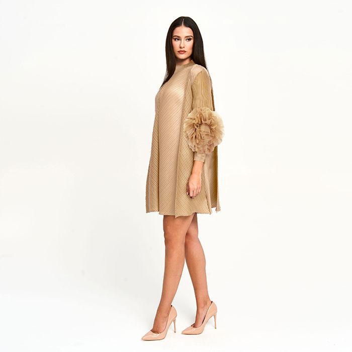 Woman wearing a beige dress with a floral accessory on a white background