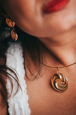 Load image into Gallery viewer, Close-up of a person wearing a gold necklace with a spiral pendant.
