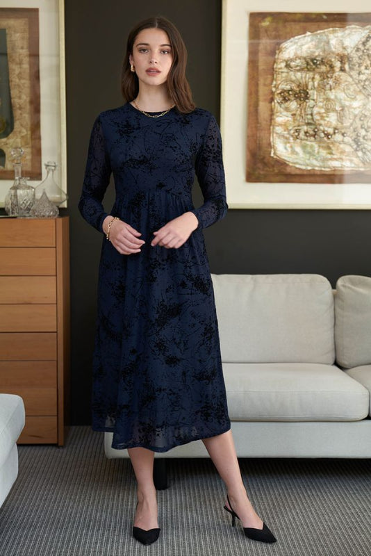 Woman wearing a dark blue  mesh and velvet dress with long sleeves, standing against a white background.