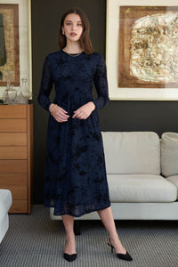 Woman wearing a dark blue  mesh and velvet dress with long sleeves, standing against a white background.