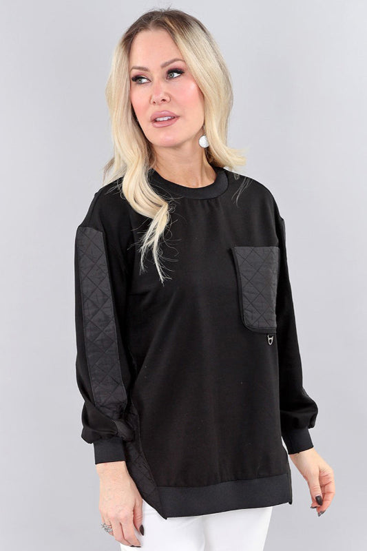 Woman wearing a black sweater with quilted sleeves on a gray background