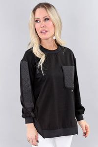 Woman wearing a black sweater with quilted sleeves on a gray background