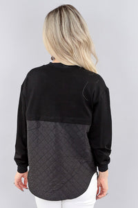 Person wearing a black long-sleeve top with a quilted design on a gray background