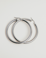 Load image into Gallery viewer, Pair of silver hoop earrings on a light gray background
