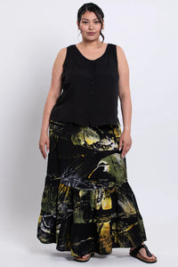 Woman wearing a black sleeveless tank and a long, batik skirt on a white background