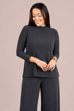 Load image into Gallery viewer, A woman modeling a dark charcoal gray three-piece knit set consisting of a mock neck long-sleeve top, matching wide-leg pants, and a coordinating belt, set against a solid dusty pink background.
