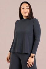 Load image into Gallery viewer, A woman modeling a dark charcoal gray long-sleeve mock neck top and matching dark gray pants against a solid light beige background.
